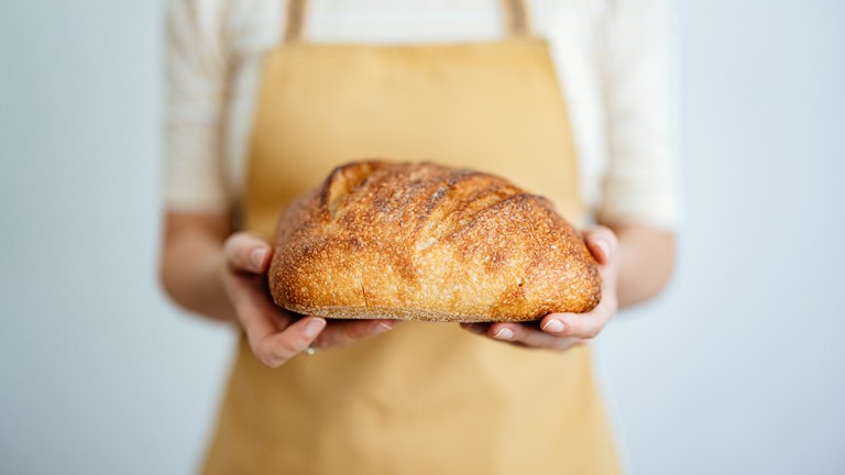 person wearing apron holding bread